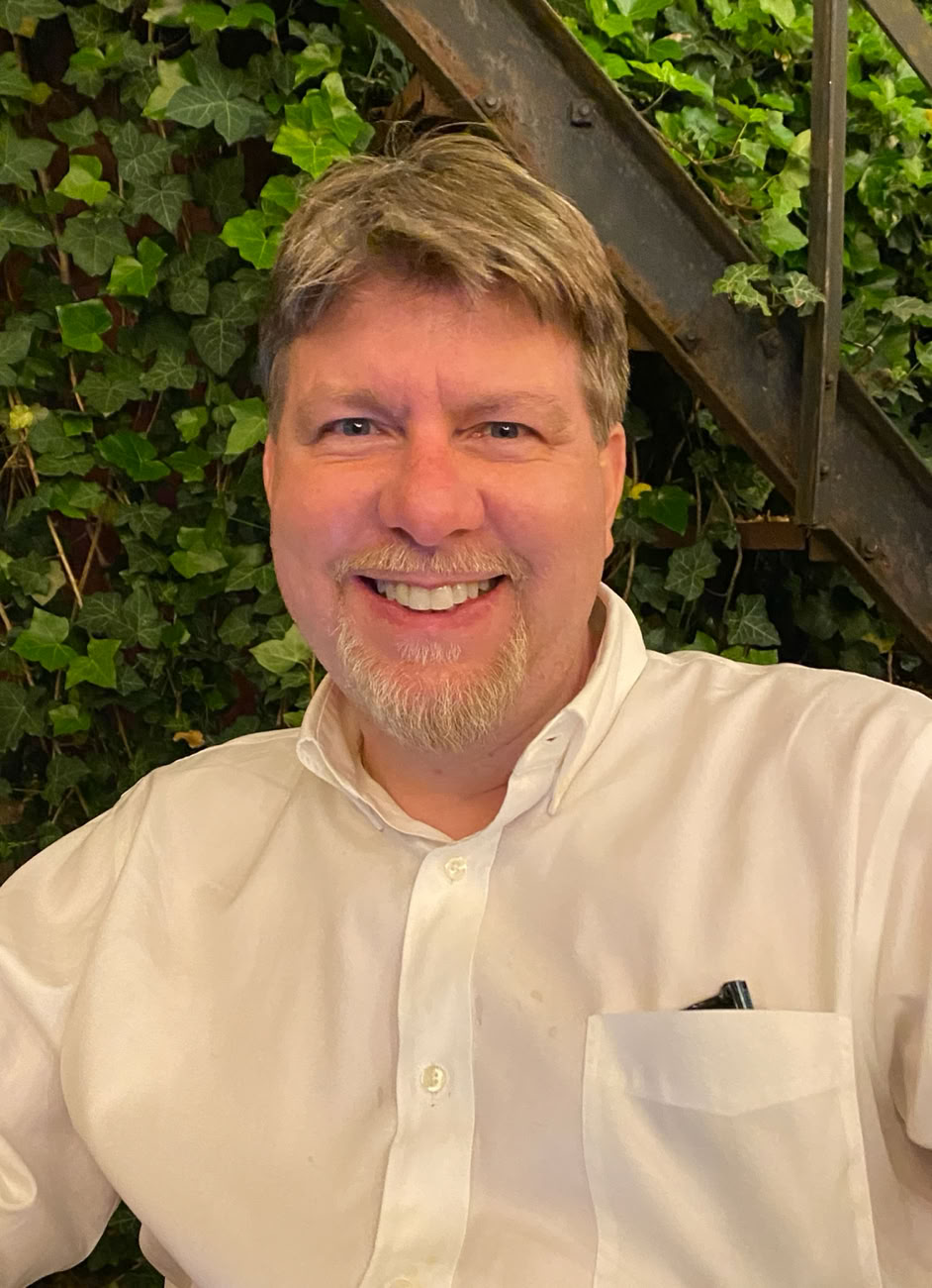 Picture of Bill Kirkpatrick, a smiling white male with short blond hair and a goatee, wearing a green t-shirt and jacket.