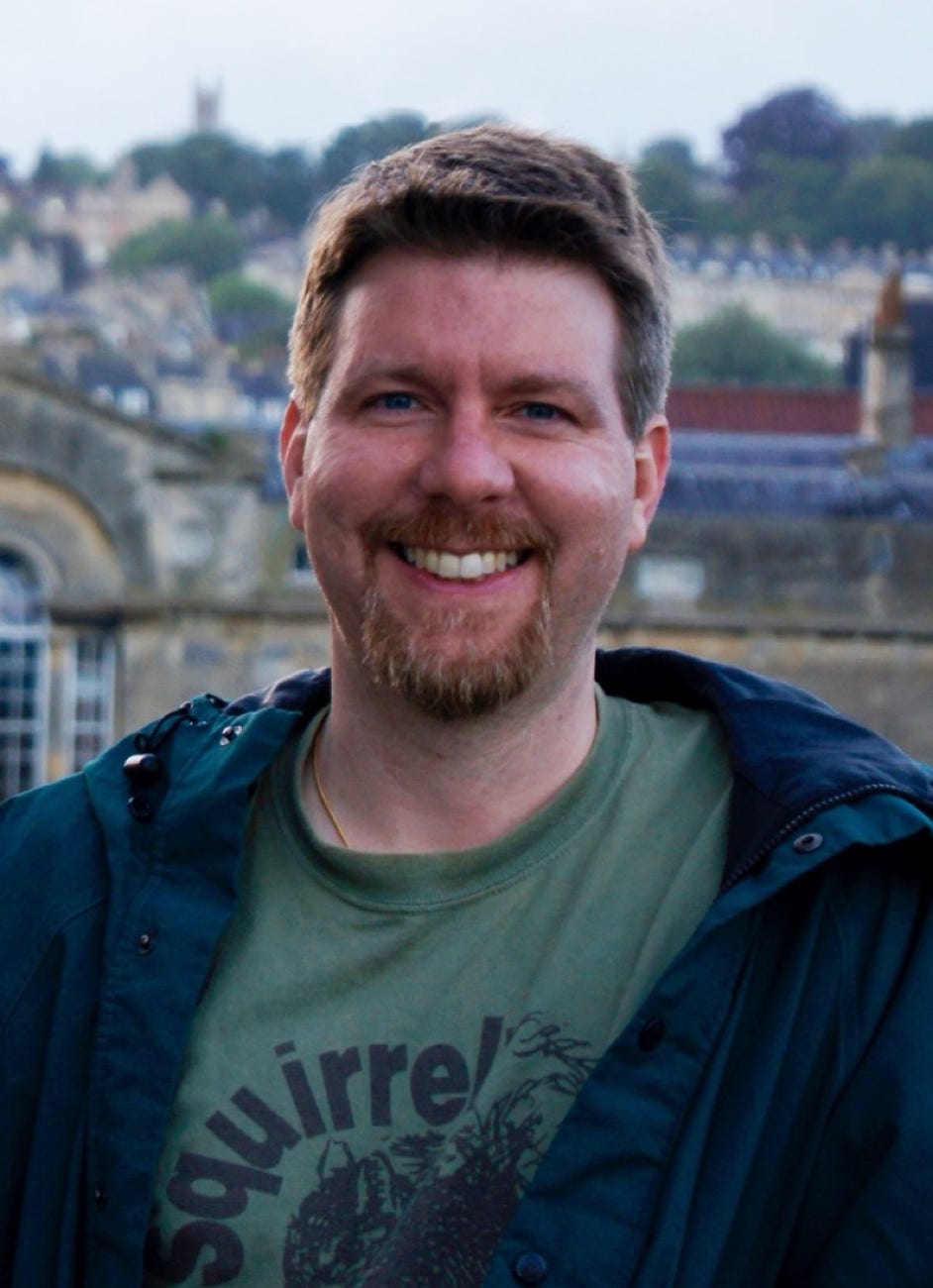 Picture of Bill Kirkpatrick, a smiling white male with short blond hair and a goatee, wearing a green t-shirt and jacket.